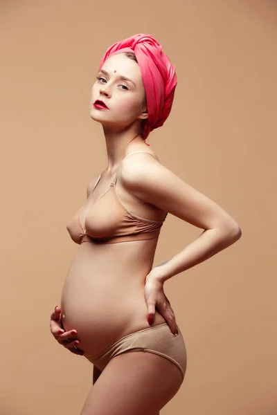Νέα όμορφη έγκυος γυναίκα που ποζάρει σε καφέ φόντο — Φωτογραφία Αρχείου