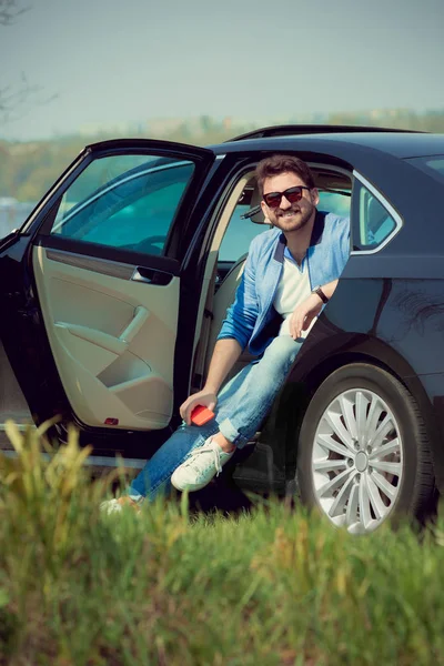 英俊的微笑男子坐在他的车与打开的门 — 图库照片