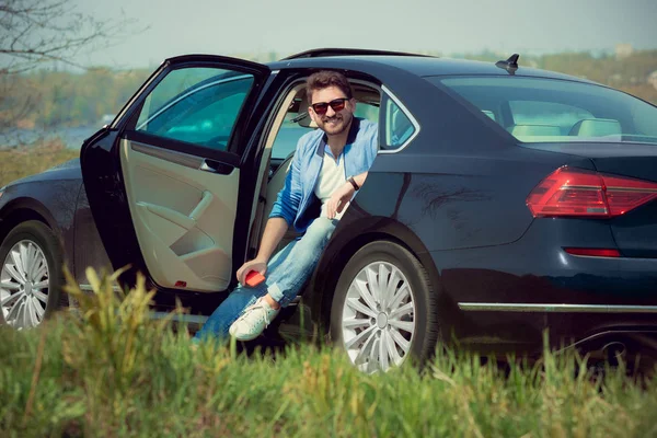 Handsome smiling man sitting in his car with opened doors — Stock Photo, Image