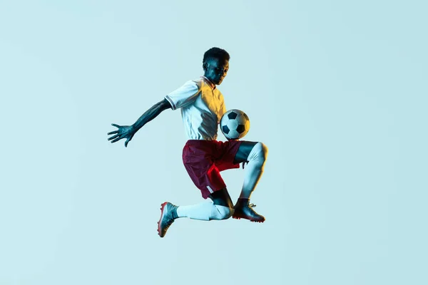 Male soccer player kicking ball in jump isolated on gradient background