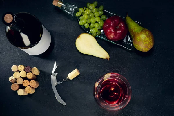Uma garrafa e um copo de vinho tinto com frutas sobre fundo de pedra escura — Fotografia de Stock