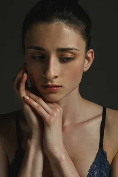 Half-length portrait of young sad woman on dark studio background