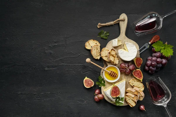 Due bicchieri di vino rosso e piatto di formaggio con frutta sulla pietra nera — Foto Stock