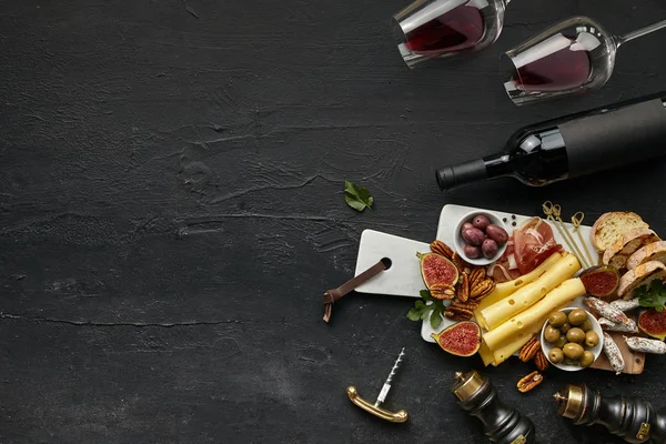 Due bicchieri di vino rosso e piatto di formaggio con frutta sulla pietra nera — Foto Stock