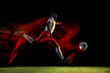 Erkek futbolcu karışık ışıkta koyu arka planda topa tekme