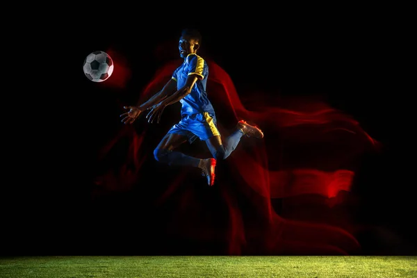 Jogador de futebol masculino chutando bola no fundo escuro em luz mista — Fotografia de Stock