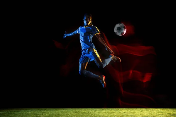 Jogador de futebol masculino chutando bola no fundo escuro em luz mista — Fotografia de Stock