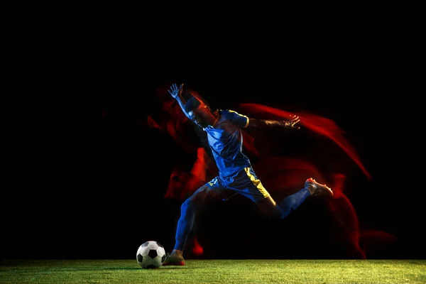 Чоловічий футболіст штовхає м'яч на темному тлі у змішаному світлі — стокове фото
