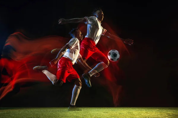 Male soccer player kicking ball on dark background in mixed light