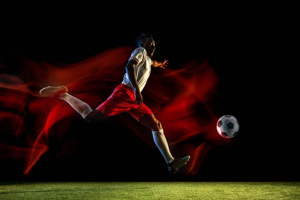 Pemain sepak bola pria menendang bola pada latar belakang gelap dalam cahaya campuran — Stok Foto