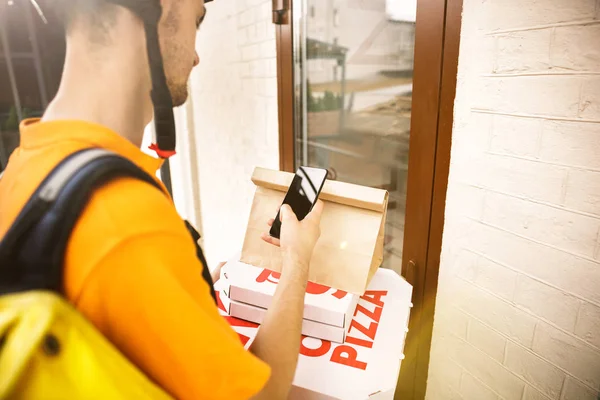 Młody człowiek jako kurier dostarczający pizzę za pomocą gadżetów — Zdjęcie stockowe