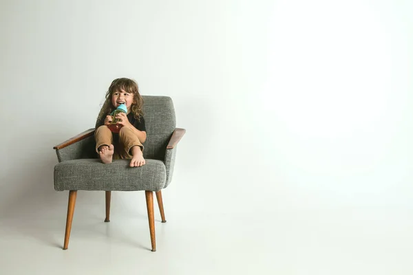 Malé dítě sedící a hrající v křesle na pozadí bílého studia — Stock fotografie