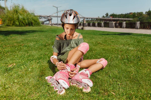 Nastoletnia dziewczyna w kasku uczy się jeździć na rolkach na zewnątrz — Zdjęcie stockowe