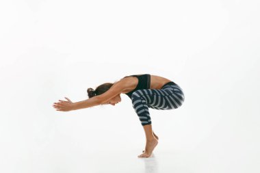 Beyaz arka planda yalnız başına yoga yapan genç bir kadın.