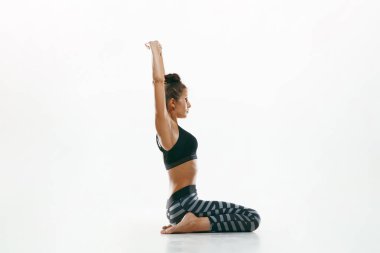 Beyaz arka planda yalnız başına yoga yapan genç bir kadın.