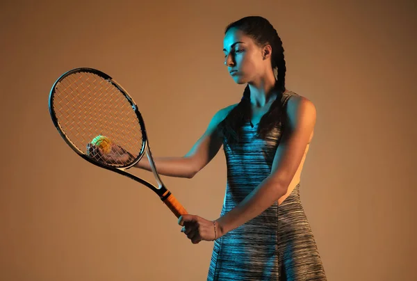 一位白人妇女在混合光线下在棕色背景上打网球 — 图库照片