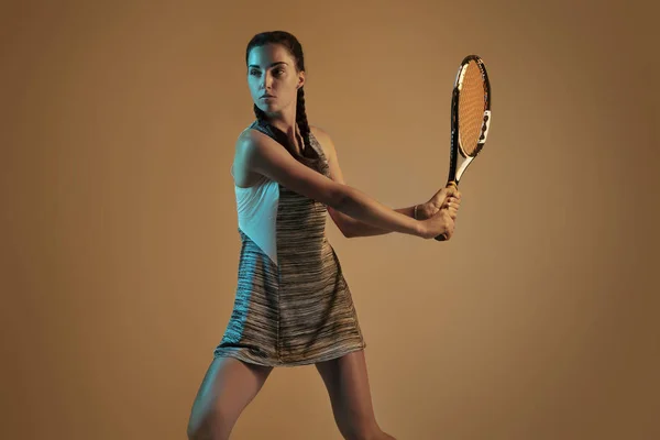 Una mujer caucásica jugando tenis sobre fondo marrón en luz mixta — Foto de Stock