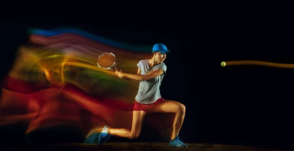 Eine kaukasische Frau spielt Tennis auf schwarzem Hintergrund in gemischtem Licht — Stockfoto