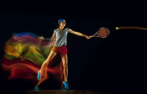 Eine kaukasische Frau spielt Tennis auf schwarzem Hintergrund in gemischtem Licht — Stockfoto