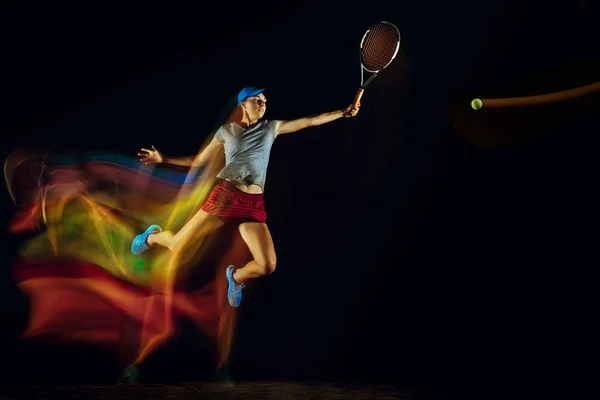 Eine kaukasische Frau spielt Tennis auf schwarzem Hintergrund in gemischtem Licht — Stockfoto