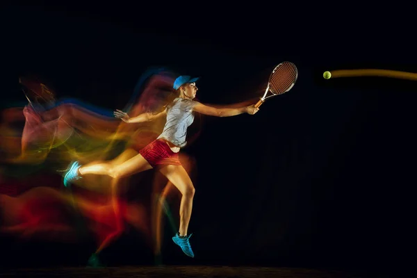 一位白人妇女在混合光线下在黑色背景上打网球 — 图库照片