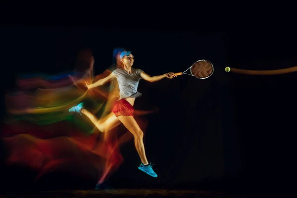 En kaukasisk kvinna som spelar tennis på svart bakgrund i blandat ljus — Stockfoto