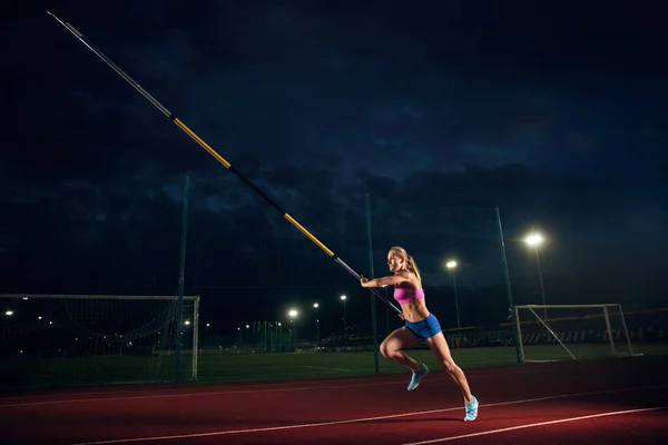 Feminino pole vaulter treinando no estádio à noite — Fotografia de Stock