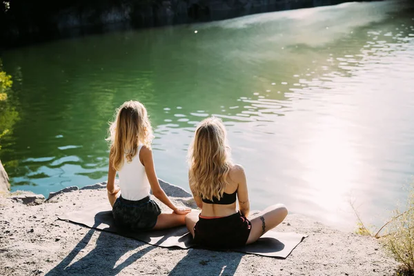 Молодые лесбиянки занимаются йогой на берегу реки в солнечный день — стоковое фото