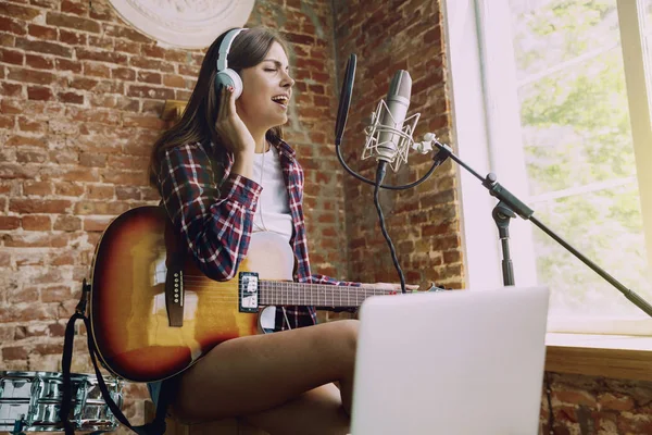 Woman recording music, playing guitar and singing at home