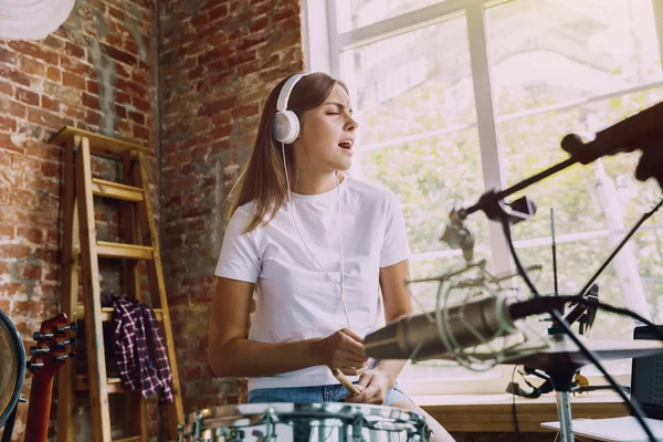 Woman recording music, playing drums and singing at home