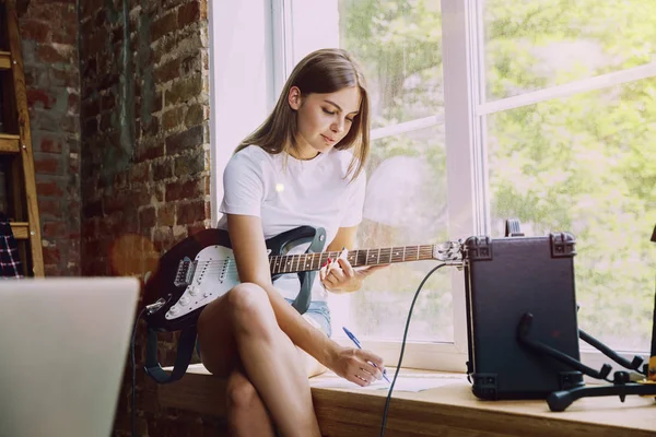 Woman recording music, playing guitar and singing at home