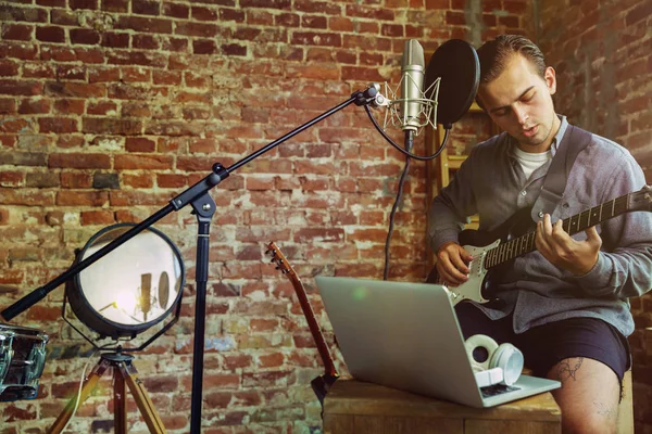 Young man recording music, playing guitar and singing at home