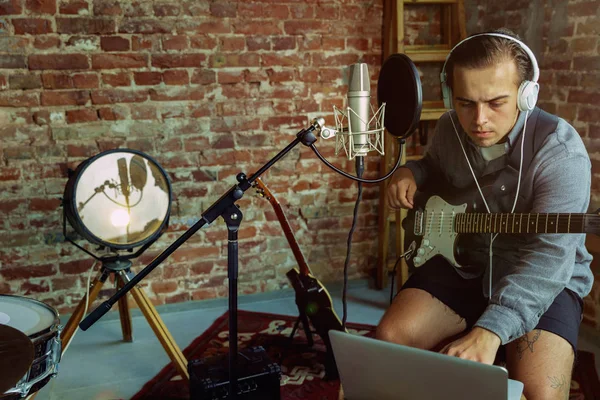 Young man recording music, playing guitar and singing at home