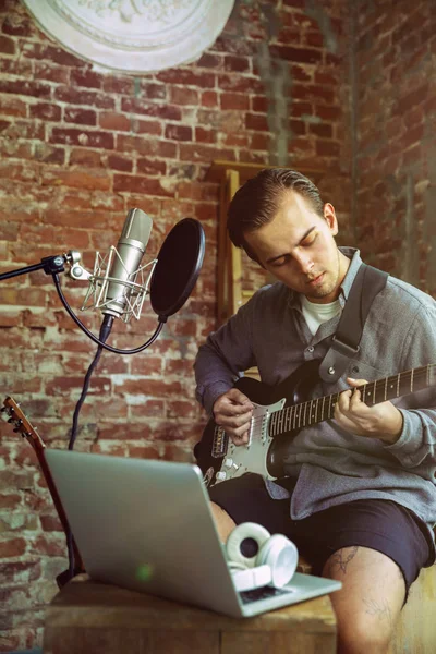 Young man recording music, playing guitar and singing at home