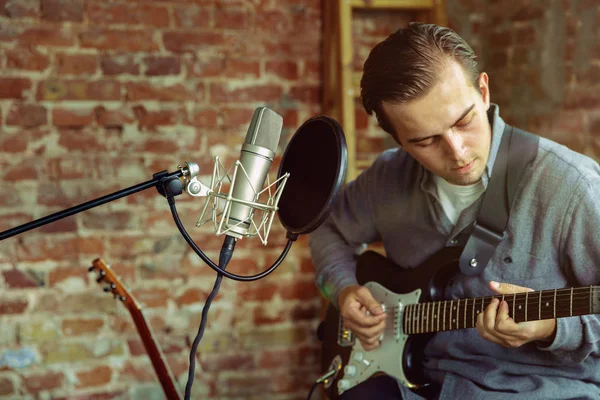 Young man recording music, playing guitar and singing at home