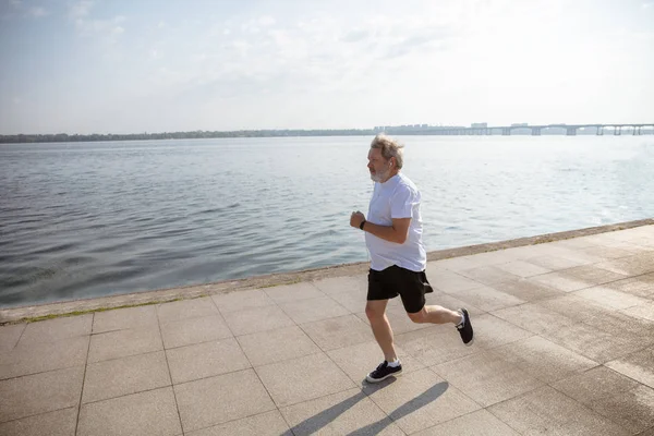 Homem sênior como corredor com braçadeira ou rastreador de fitness na beira do rio — Fotografia de Stock