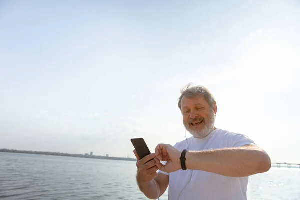 Senior man as runner with armband or fitness tracker at the riverside — Stock Photo, Image