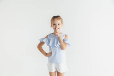 Beyaz stüdyo arka planda rahat giysiler içinde poz veren küçük gülümseyen kız