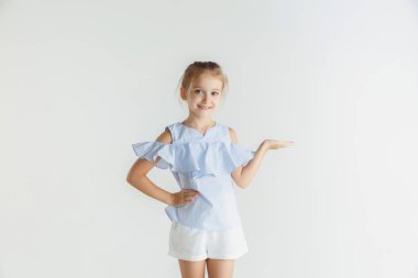 Beyaz stüdyo arka planda rahat giysiler içinde poz veren küçük gülümseyen kız