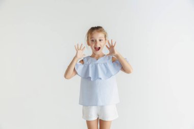 Beyaz stüdyo arka planda rahat giysiler içinde poz veren küçük gülümseyen kız