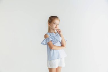 Beyaz stüdyo arka planda rahat giysiler içinde poz veren küçük gülümseyen kız