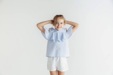 Beyaz stüdyo arka planda rahat giysiler içinde poz veren küçük gülümseyen kız