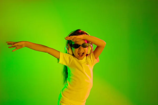 Retrato de menina em fones de ouvido no fundo verde em luz de néon — Fotografia de Stock