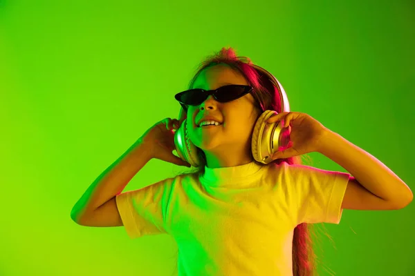 Porträt eines kleinen Mädchens mit Kopfhörern auf grünem Hintergrund im Neonlicht — Stockfoto
