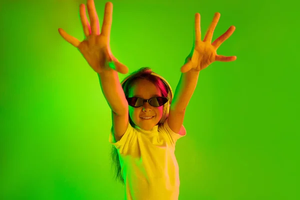 Portret van klein meisje in koptelefoon op groene achtergrond in neon licht — Stockfoto