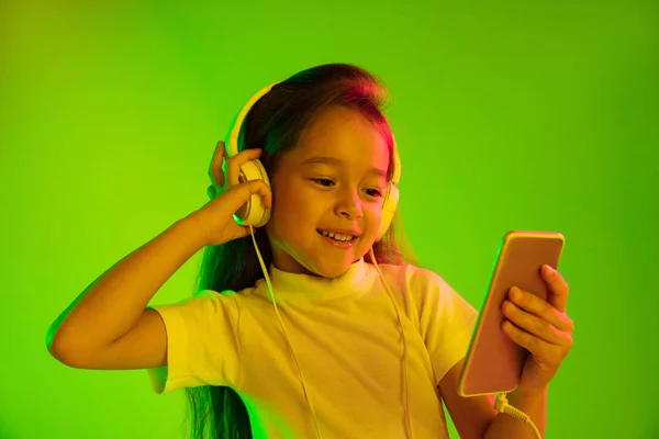 Πορτρέτο του μικρού κοριτσιού στα ακουστικά σε πράσινο φόντο στο φως νέον — Φωτογραφία Αρχείου