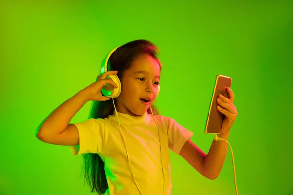 Πορτρέτο του μικρού κοριτσιού στα ακουστικά σε πράσινο φόντο στο φως νέον — Φωτογραφία Αρχείου