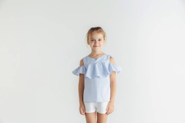 Beyaz stüdyo arka planda rahat giysiler içinde poz veren küçük gülümseyen kız