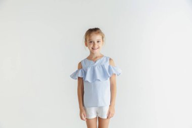 Beyaz stüdyo arka planda rahat giysiler içinde poz veren küçük gülümseyen kız