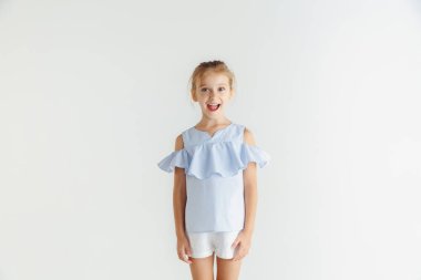 Beyaz stüdyo arka planda rahat giysiler içinde poz veren küçük gülümseyen kız